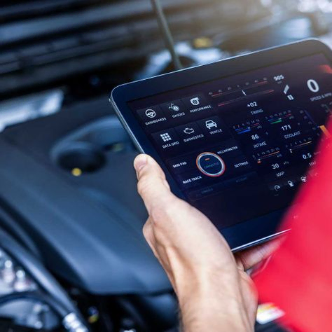 Kfz-Servicemechaniker nutzt digitales Tablet mit Diagnosesoftware, um den Motorzustand zu überprüfen. Fahrzeuginspektion